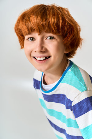 A cheerful little boy with vibrant orange hair wears a striped shirt.