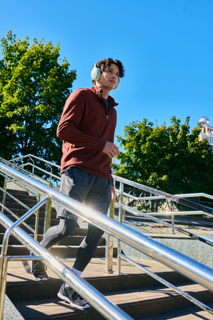 A young man with curly hair confidently walks outside in a sporty jacket on a spring day.