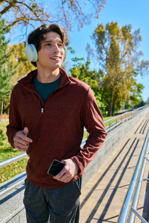 A young man with curly hair jogs happily in a sport jacket on a sunny spring day.
