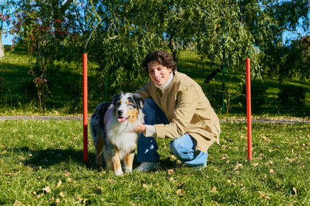 Young man with curly hair enjoys his day in spring, playing with his Australian Shepherd dog.