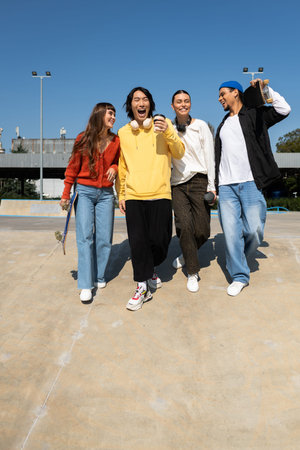 Four young friends laugh and stroll along a sunny path, enjoying each others company and drinks.