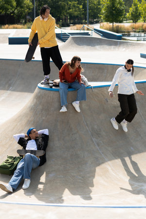 Five friends relax and laugh at a skate park, sharing joyful moments in the warm sunlight.の写真素材