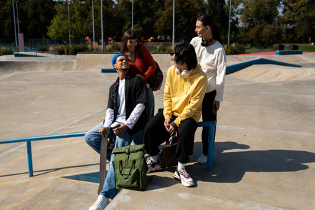A group of friends laughs and chats at an outdoor skate park under clear blue skies.