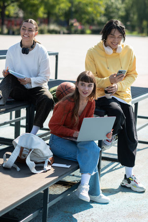 Three friends share smiles while working on their laptops outdoors, embracing friendship and fun.