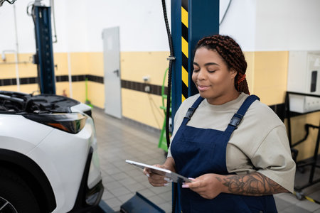 Young African American female mechanic reviews car maintenance tasks in a modern garageの写真素材