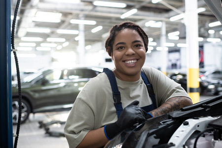 Dedicated female mechanic smiles while working on a car in a busy auto repair shop.
