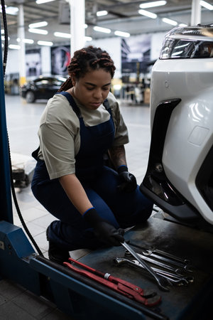 A talented young woman in overalls focuses on car maintenance in a busy garage setting.