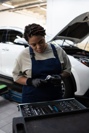 African American woman in overalls focused on car maintenance while working in the garageの写真素材