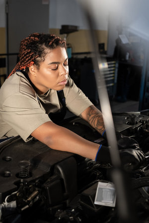 Dedicated female mechanic works on a car engine with focus and skill in a vibrant garage.の写真素材