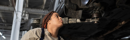 Young Black female mechanic inspects a car with focus and determination in a garage, banner