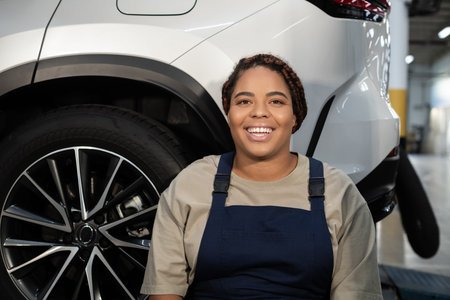 A young African American woman enjoys her work as a mechanic in a busy auto repair shop.