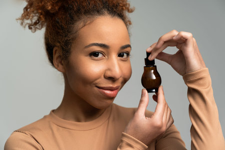 A young woman with curly hair holds an elegant skincare bottle, radiating confidence and charm.