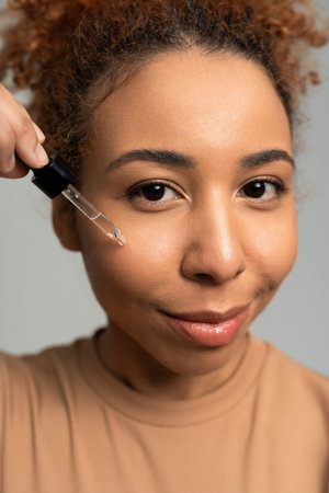 A young woman smiles joyfully as she applies serum, enhancing her radiant skin.の写真素材