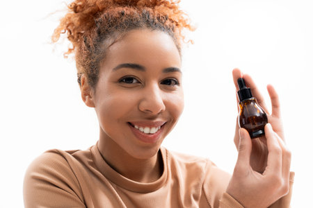Beautiful young woman holds a bottle of skin oil, radiating confidence and joy.