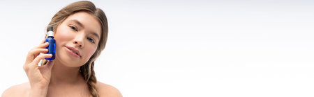 A young woman radiates beauty while gently applying serum to her face in a calm setting.