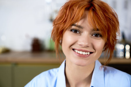 Bright and cheerful young woman with stunning red hair smiles warmly while relaxing at home.