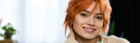 A cheerful young woman with stunning red hair enjoys a peaceful afternoon at home, radiating joy.の写真素材