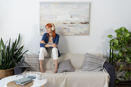 Young woman with red hair relaxes in her contemporary living room, immersed in thought.