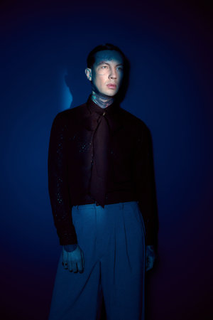 A stylish man poses against a vibrant blue backdrop, exuding confidence and charm in trendy attire.の写真素材