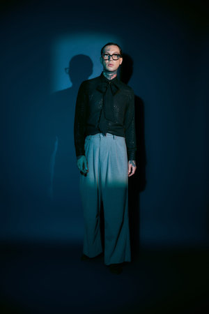 A handsome man with a sleek outfit and glasses showcases modern fashion in a dramatic setting.の写真素材