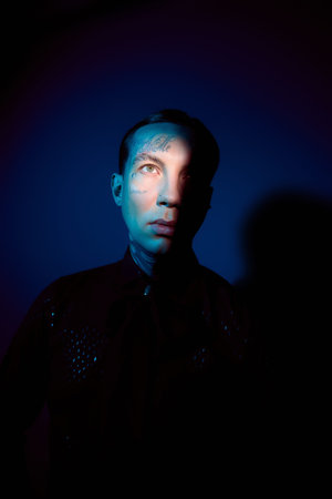 Stylish young man poses confidently, highlighted by intriguing lighting in a creative setting.
