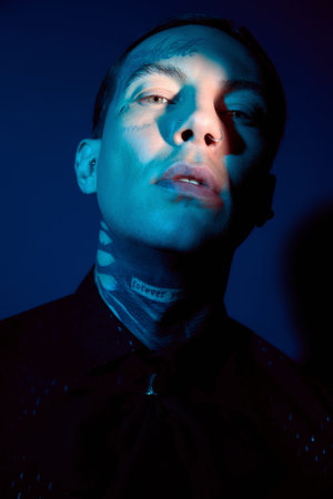 A young man showcases his unique style with bold tattoos under vibrant lighting, exuding confidence.の写真素材