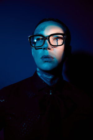 Handsome young man showcases unique fashion and intense gaze in striking blue lighting.