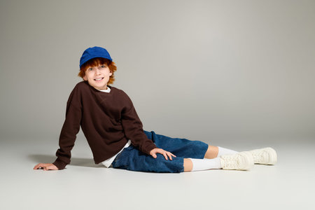A cheerful boy with red hair relaxes in a casual outfit, showcasing child fashion in style.
