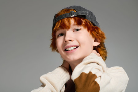 Excited redhead boy smiles warmly while showcasing trendy casual clothes in studio setting