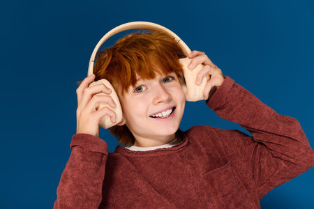 Young boy with red hair smiles while wearing stylish headphones in a vibrant studio setting.