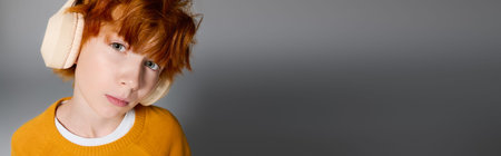 Redhead boy in trendy outfit poses playfully in a contemporary grey studio, bannerの写真素材