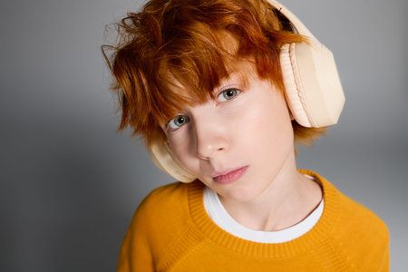 Redhead boy in cozy yellow sweater poses confidently with headphones in a modern studio.