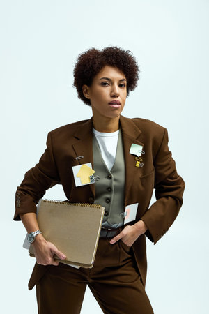 A confident young woman in elegant attire stands proudly with a notepad, exuding modern fashion.