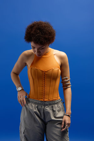 Stylish young woman wears a striking orange top and relaxed pants, exuding confidence and charm.