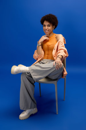 A young beautiful woman showcases her fashion sense in elegant attire, seated gracefully on a chair.