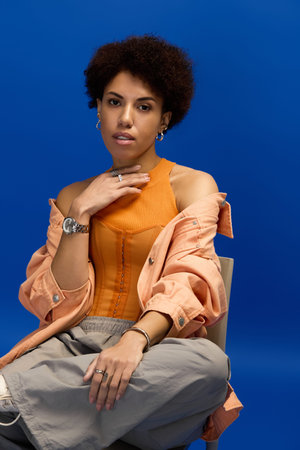 Stylish young woman in elegant attire poses confidently against a bright blue backdrop.