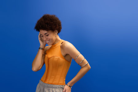 A young beautiful woman in elegant attire enjoys a lively moment against a bold blue backdrop.