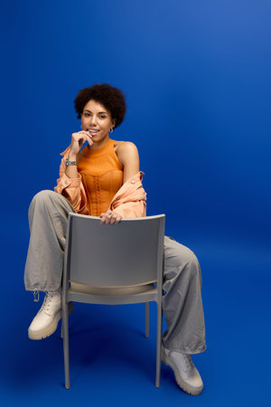 Confident young woman in elegant attire poses against a bright blue backdrop, exuding style.