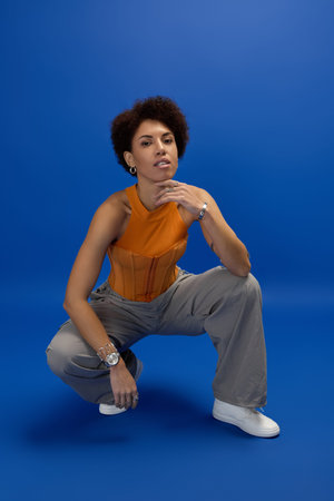 Confident young woman showcases stylish attire, exuding beauty against a vibrant blue backdrop.