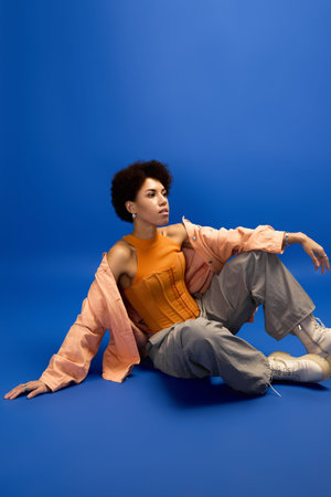 A stylish young woman poses gracefully against a vibrant blue background.