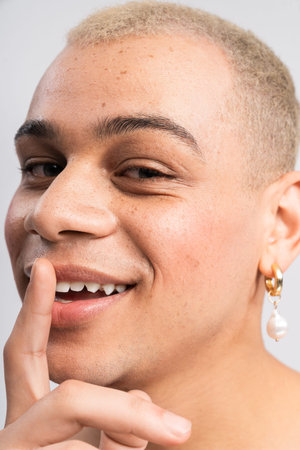 Handsome fashion forward man smiles warmly while playfully gesturing with his finger on his lips.