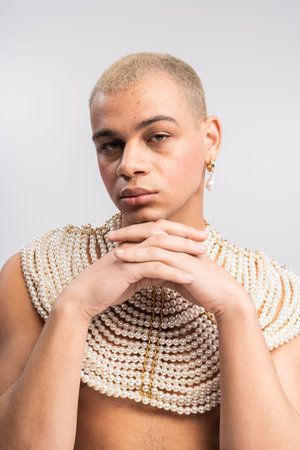 Handsome stylish man showcases a unique look with pearls and a striking pose in a creative space.の写真素材