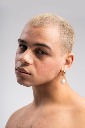 Handsome man poses elegantly, highlighting his striking features and stylish earring in soft light.