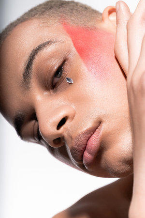 A stylish man with unique makeup poses confidently in a creative studio.