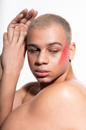 Handsome man showcases fashion artistry with vibrant facial makeup and a captivating gaze.の写真素材
