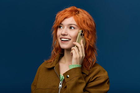 Young woman with red hair smiles on the phone in stylish spring attire.