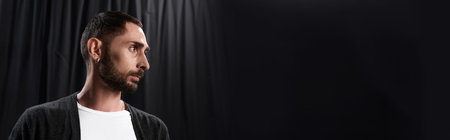 In a theater space, a handsome man stands thoughtfully, preparing for his next captivating role.
