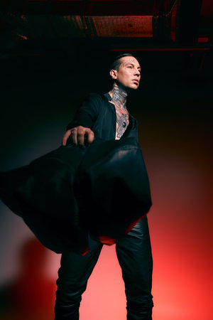 A handsome young man stands boldly, showcasing his stylish outfit amid dramatic lighting.