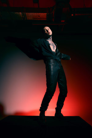 This stylish man poses on a platform, showcasing his edgy fashion against a bold backdrop.