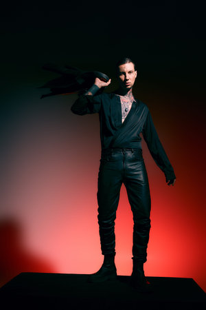 A handsome young adult stands confidently, showcasing a stylish outfit against a vivid backdrop.